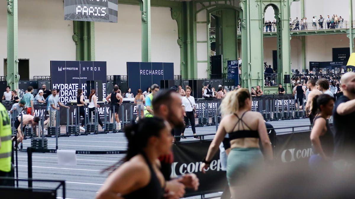 Hyrox athlete running during competition with functional fitness stations in the background
